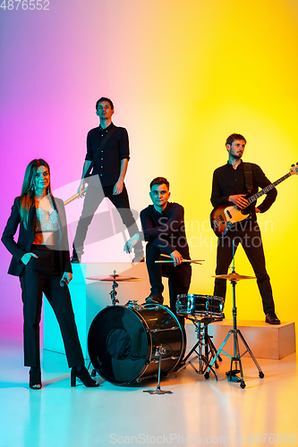 Image of Young caucasian musicians, band performing in neon light on gradient studio background