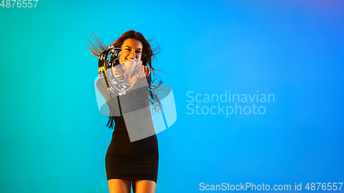 Image of Caucasian female singer with tambourin isolated on blue studio background in neon light