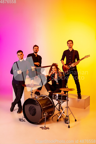 Image of Young caucasian musicians, band performing in neon light on gradient studio background