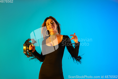 Image of Caucasian female singer with tambourin isolated on blue studio background in neon light