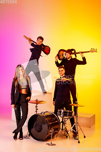 Image of Young caucasian musicians, band performing in neon light on gradient studio background