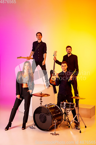 Image of Young caucasian musicians, band performing in neon light on gradient studio background