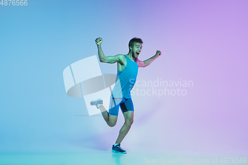 Image of Full length portrait of active young caucasian running, jogging man on gradient studio background in neon light