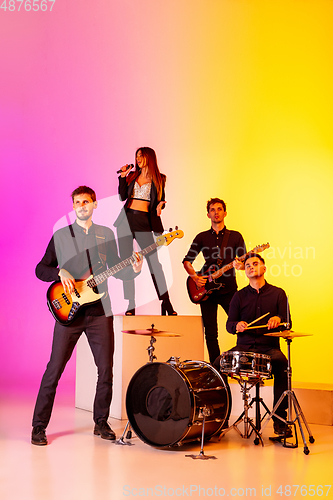 Image of Young caucasian musicians, band performing in neon light on gradient studio background