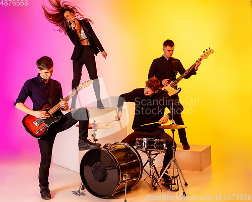 Image of Young caucasian musicians, band performing in neon light on gradient studio background