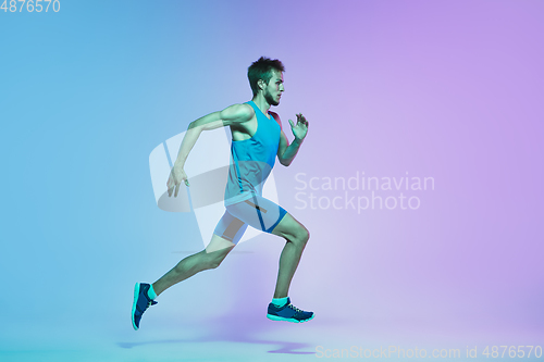 Image of Full length portrait of active young caucasian running, jogging man on gradient studio background in neon light