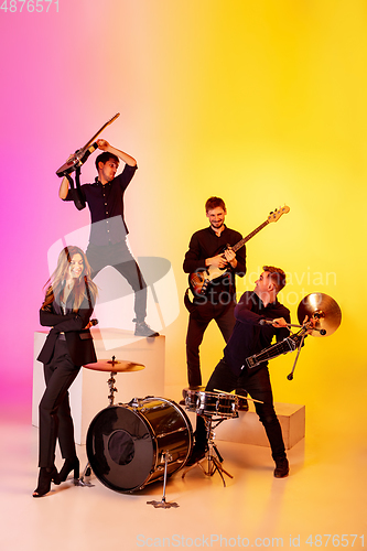 Image of Young caucasian musicians, band performing in neon light on gradient studio background