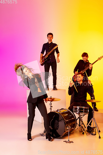 Image of Young caucasian musicians, band performing in neon light on gradient studio background
