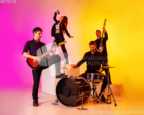 Image of Young caucasian musicians, band performing in neon light on gradient studio background