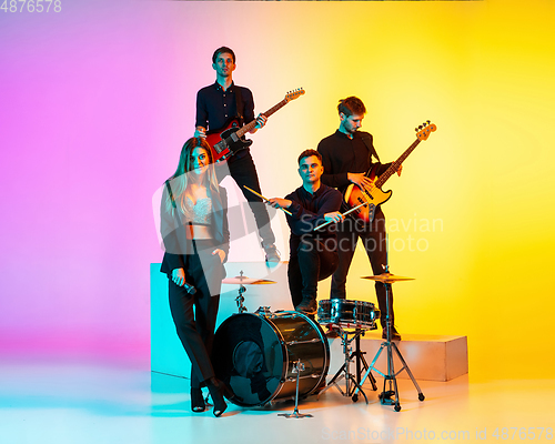 Image of Young caucasian musicians, band performing in neon light on gradient studio background