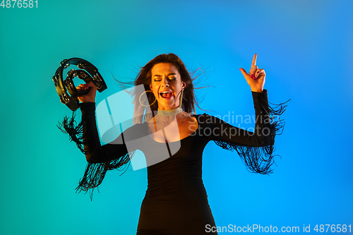 Image of Caucasian female singer with tambourin isolated on blue studio background in neon light