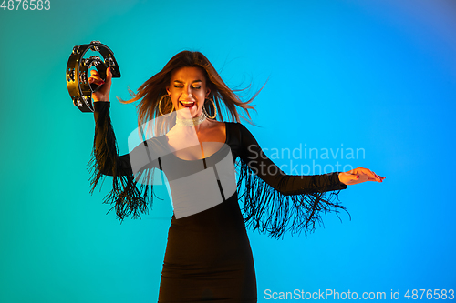 Image of Caucasian female singer with tambourin isolated on blue studio background in neon light