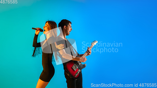 Image of Caucasian musicians, singer and guitarist, isolated on blue studio background in neon light