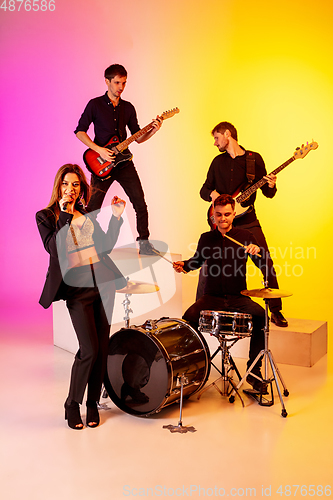 Image of Young caucasian musicians, band performing in neon light on gradient studio background