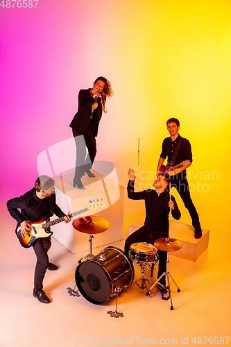 Image of Young caucasian musicians, band performing in neon light on gradient studio background