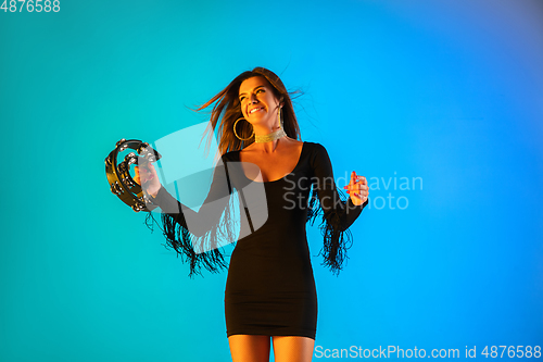 Image of Caucasian female singer with tambourin isolated on blue studio background in neon light