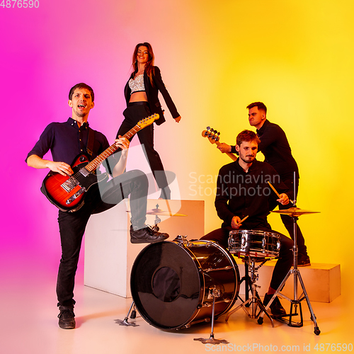 Image of Young caucasian musicians, band performing in neon light on gradient studio background