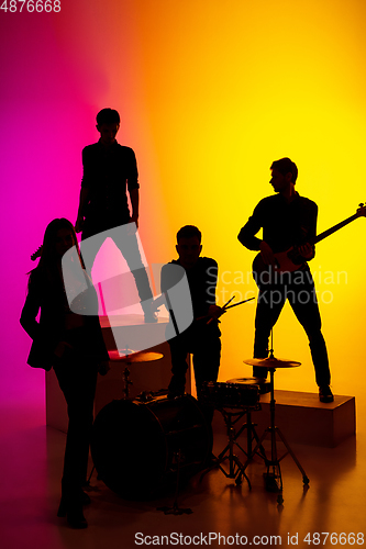 Image of Young caucasian musicians, band performing in neon light on gradient studio background