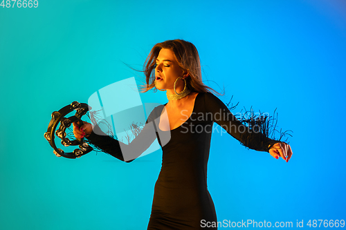 Image of Caucasian female singer with tambourin isolated on blue studio background in neon light