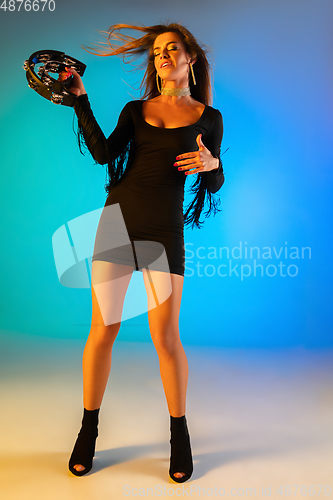 Image of Caucasian female singer with tambourin isolated on blue studio background in neon light