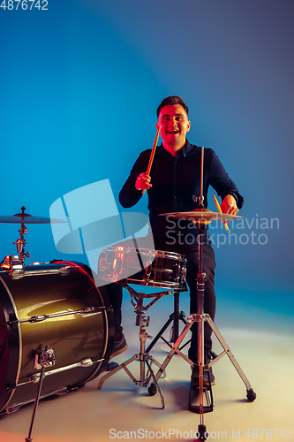 Image of Caucasian male drummer improvising isolated on blue studio background in neon light