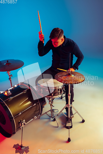 Image of Caucasian male drummer improvising isolated on blue studio background in neon light