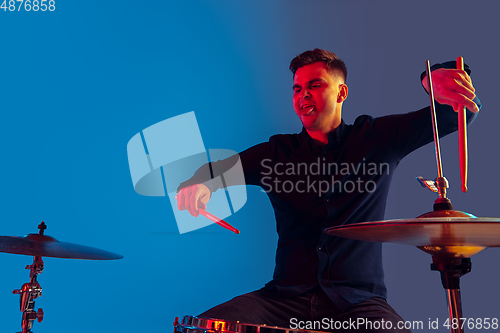 Image of Caucasian male drummer improvising isolated on blue studio background in neon light