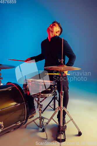 Image of Caucasian male drummer improvising isolated on blue studio background in neon light