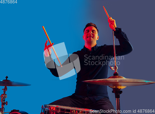 Image of Caucasian male drummer improvising isolated on blue studio background in neon light