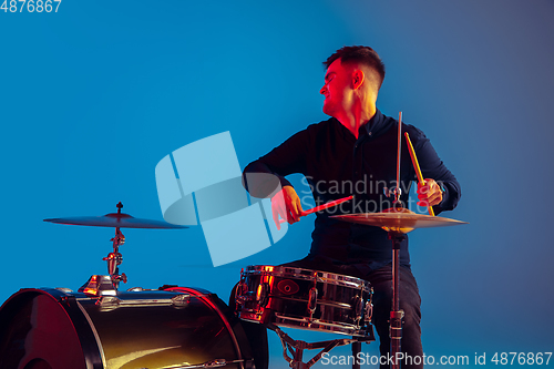 Image of Caucasian male drummer improvising isolated on blue studio background in neon light