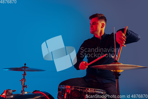 Image of Caucasian male drummer improvising isolated on blue studio background in neon light