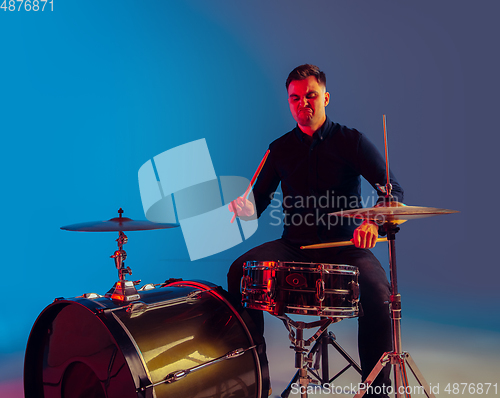 Image of Caucasian male drummer improvising isolated on blue studio background in neon light