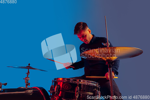 Image of Caucasian male drummer improvising isolated on blue studio background in neon light