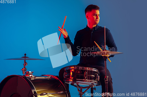 Image of Caucasian male drummer improvising isolated on blue studio background in neon light