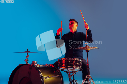 Image of Caucasian male drummer improvising isolated on blue studio background in neon light