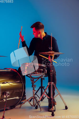 Image of Caucasian male drummer improvising isolated on blue studio background in neon light