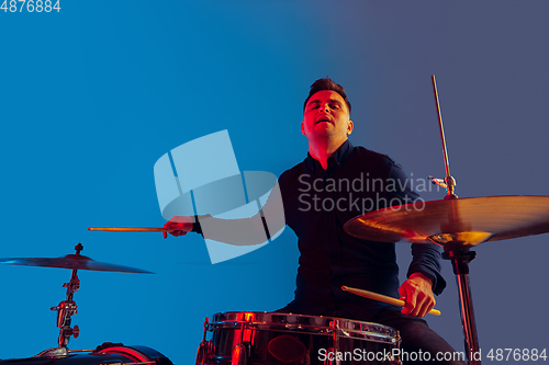 Image of Caucasian male drummer improvising isolated on blue studio background in neon light