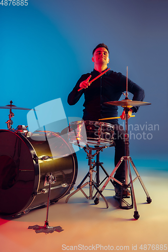 Image of Caucasian male drummer improvising isolated on blue studio background in neon light