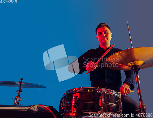 Image of Caucasian male drummer improvising isolated on blue studio background in neon light