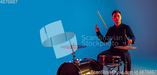 Image of Caucasian male drummer improvising isolated on blue studio background in neon light