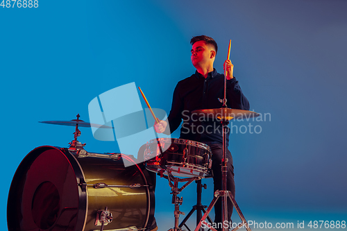 Image of Caucasian male drummer improvising isolated on blue studio background in neon light