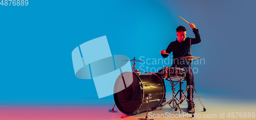 Image of Caucasian male drummer improvising isolated on blue studio background in neon light