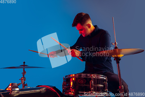 Image of Caucasian male drummer improvising isolated on blue studio background in neon light