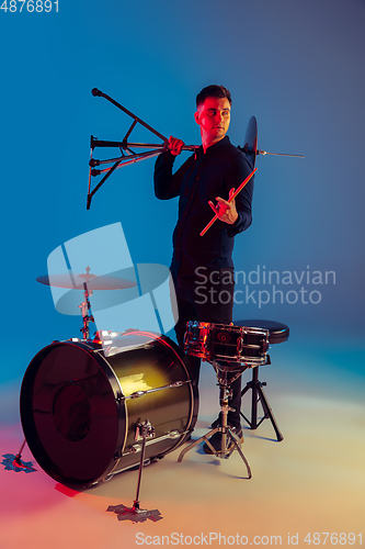 Image of Caucasian male drummer improvising isolated on blue studio background in neon light