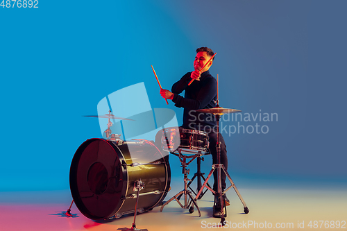 Image of Caucasian male drummer improvising isolated on blue studio background in neon light