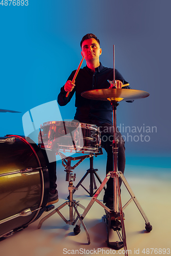 Image of Caucasian male drummer improvising isolated on blue studio background in neon light