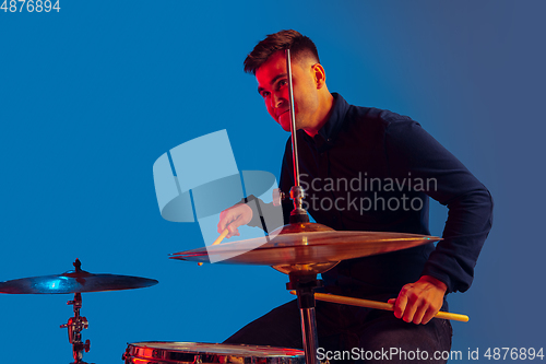 Image of Caucasian male drummer improvising isolated on blue studio background in neon light