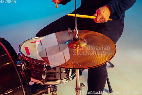 Image of Caucasian male drummer improvising isolated on blue studio background in neon light