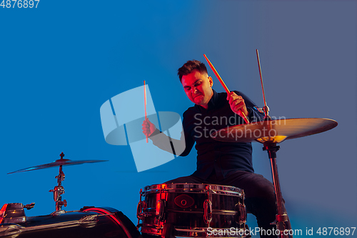 Image of Caucasian male drummer improvising isolated on blue studio background in neon light