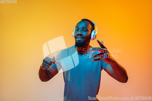 Image of African-american man\'s portrait isolated on gradient orange studio background in neon light